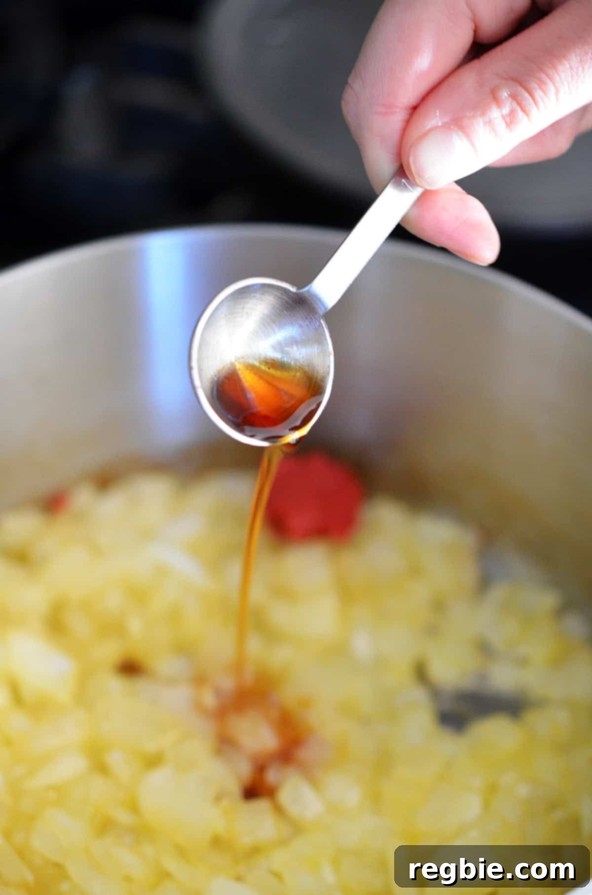 Adding a spoonful of fish sauce to a saucepan with sautéed diced onions and tomato paste.