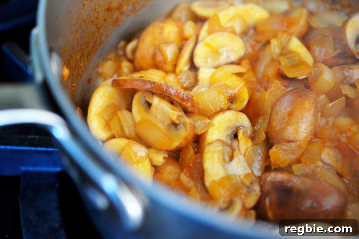 Sautéed sliced button mushrooms and diced onions are cooking in a small saucepan, the base for umami gravy.