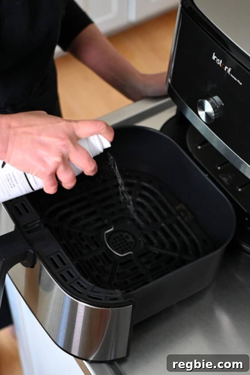 Golden Crispy Air Fried Whole Chicken 11 A hand is spraying avocado oil cooking spray into an empty air fryer basket, preparing it for cooking.