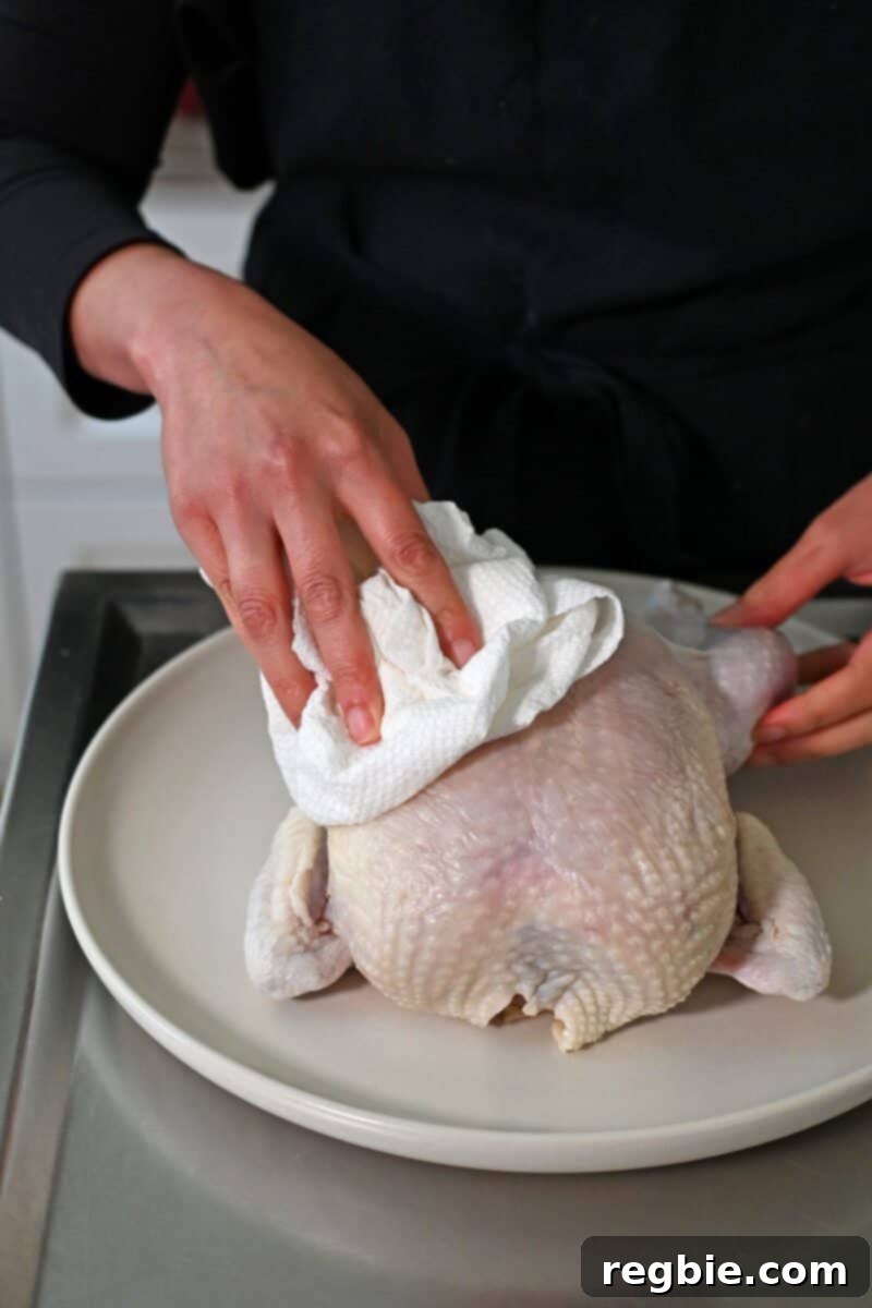 Golden Crispy Air Fried Whole Chicken 5 A whole raw chicken is being blotted dry with paper towels by two hands, preparing it for seasoning.
