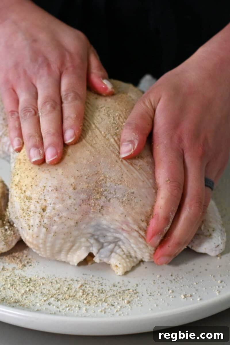 Golden Crispy Air Fried Whole Chicken 7 Two hands are meticulously rubbing a spice seasoning blend on top of a raw whole chicken, ensuring even coverage.