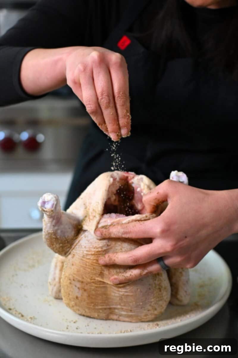 Golden Crispy Air Fried Whole Chicken 8 A hand is sprinkling seasoning blend into the cavity of a raw whole chicken, ensuring flavor permeates from within.