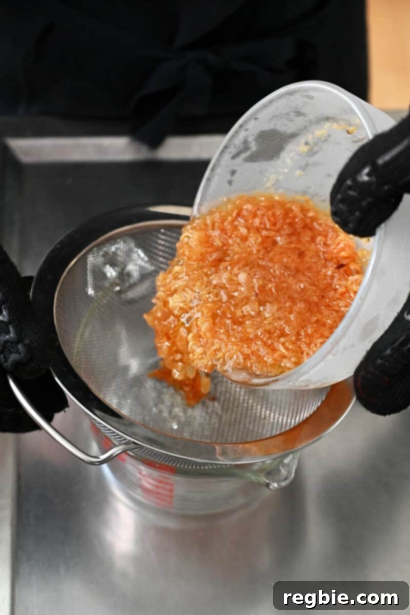 The shallots and oil mixture is being carefully poured through a fine mesh sieve into a glass bowl, separating the solids from the liquid.