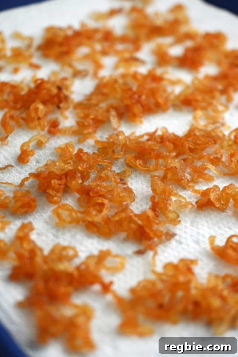 A close-up view of a tray of freshly made crispy shallots, still slightly warm and draining on paper towels.