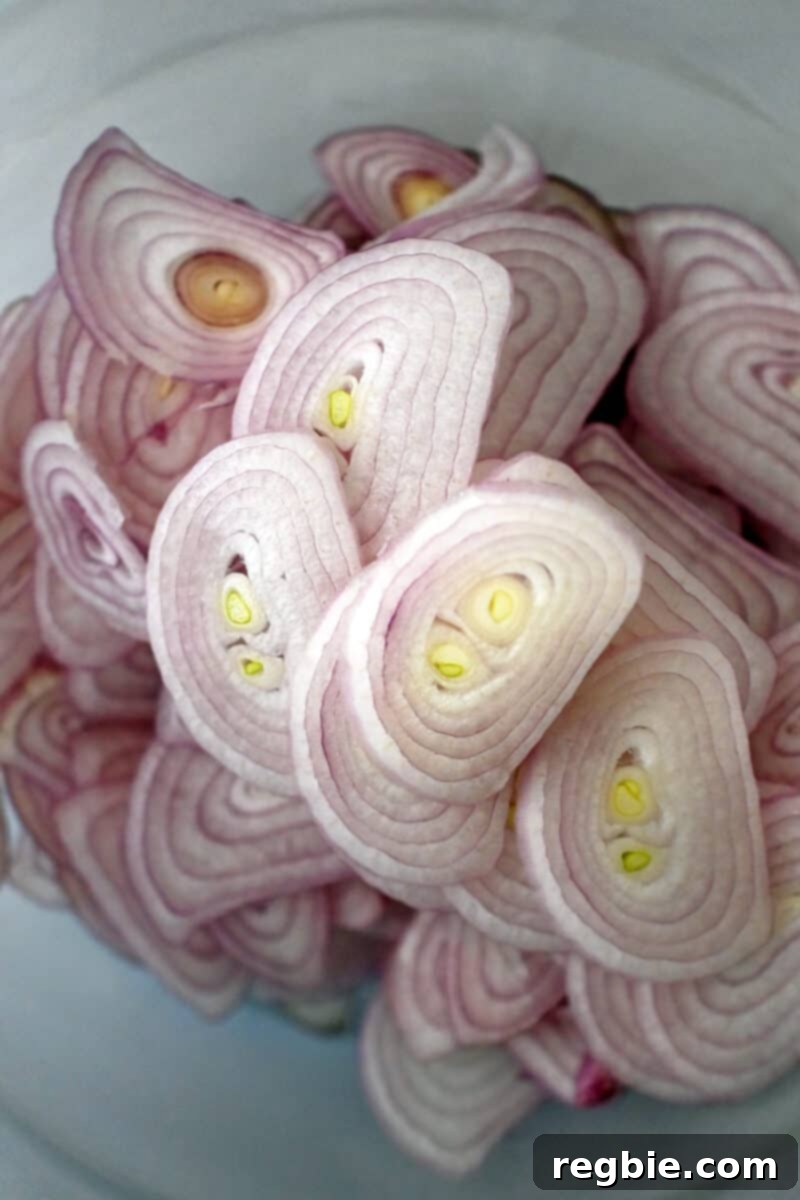 An overhead shot captures a clear glass bowl filled with thinly sliced shallots, awaiting the oil.