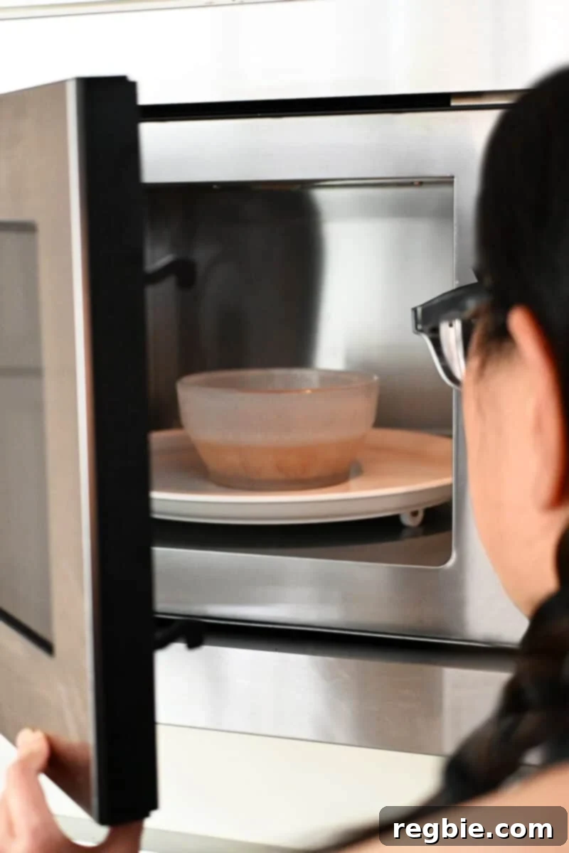 An open microwave oven reveals a bowl of sliced shallots and avocado oil inside, actively cooking.