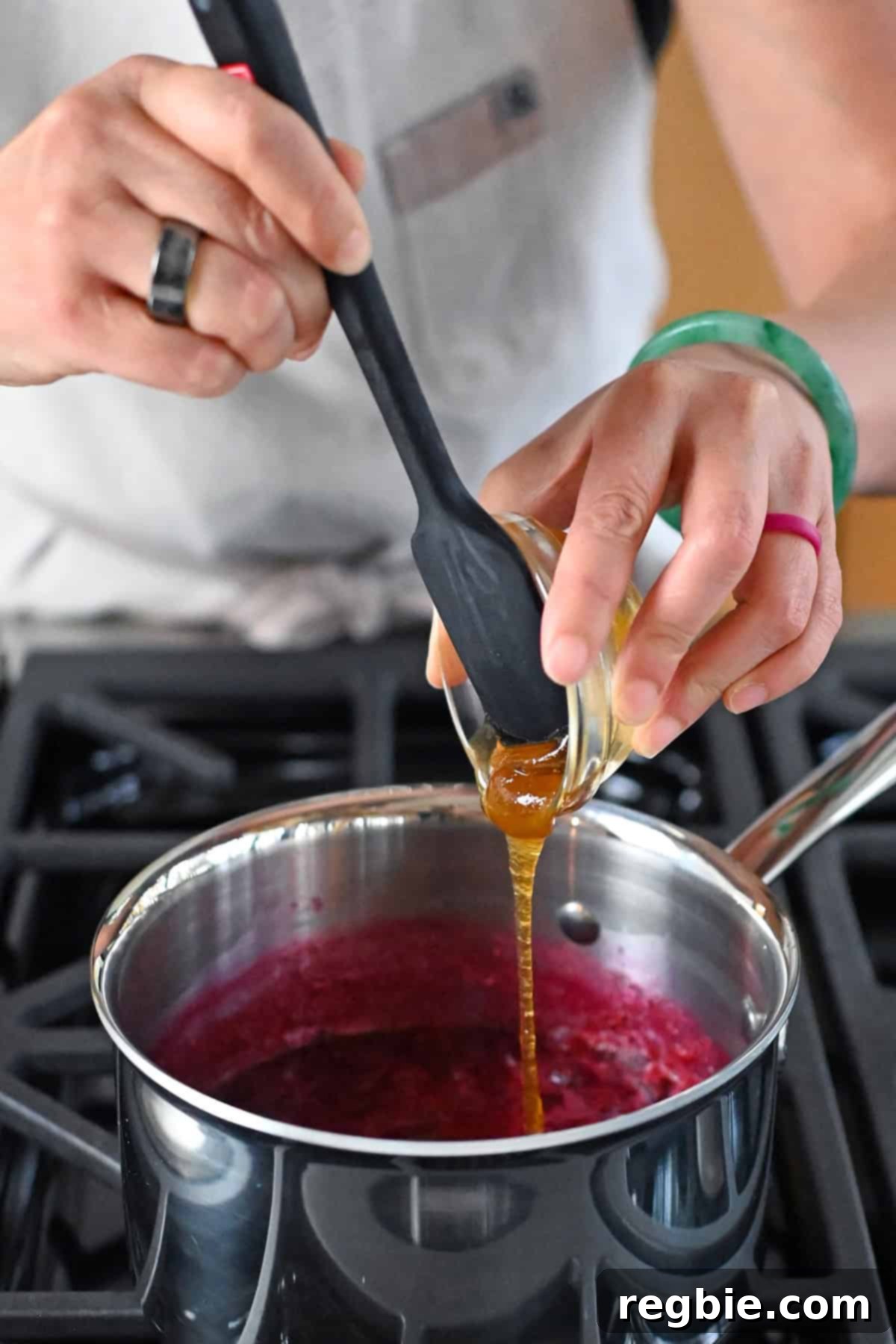 Adding honey to a saucepan filled with paleo cranberry cherry sauce, demonstrating the optional sweetness adjustment.