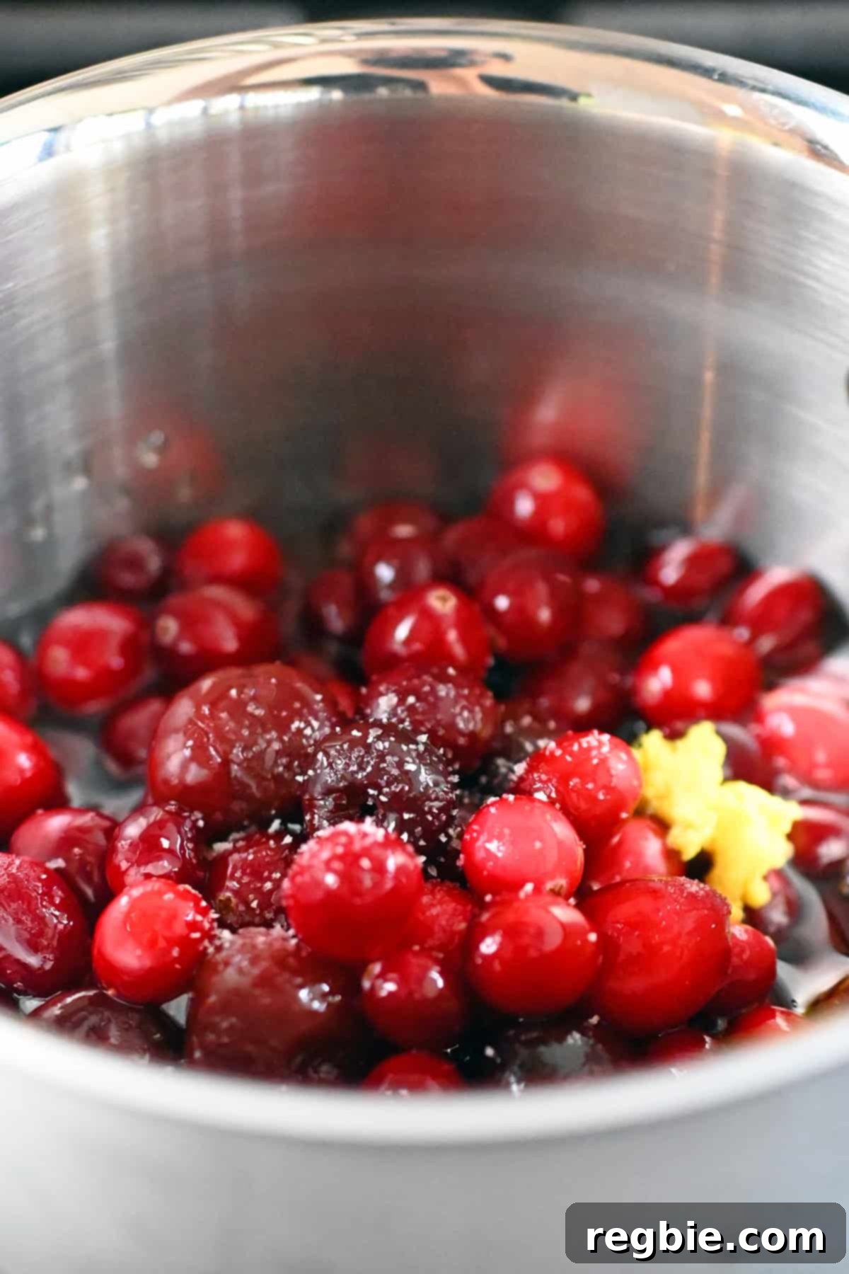 A closeup of a saucepan filled with frozen cherries, cranberries, apple juice, minced ginger, and salt, ready for simmering.