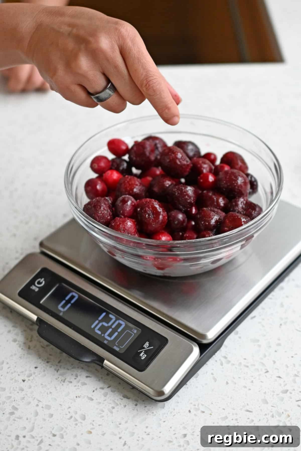 Measuring frozen cranberries and cherries in a glass bowl on a kitchen scale to make paleo cranberry sauce, highlighting the precise quantities.