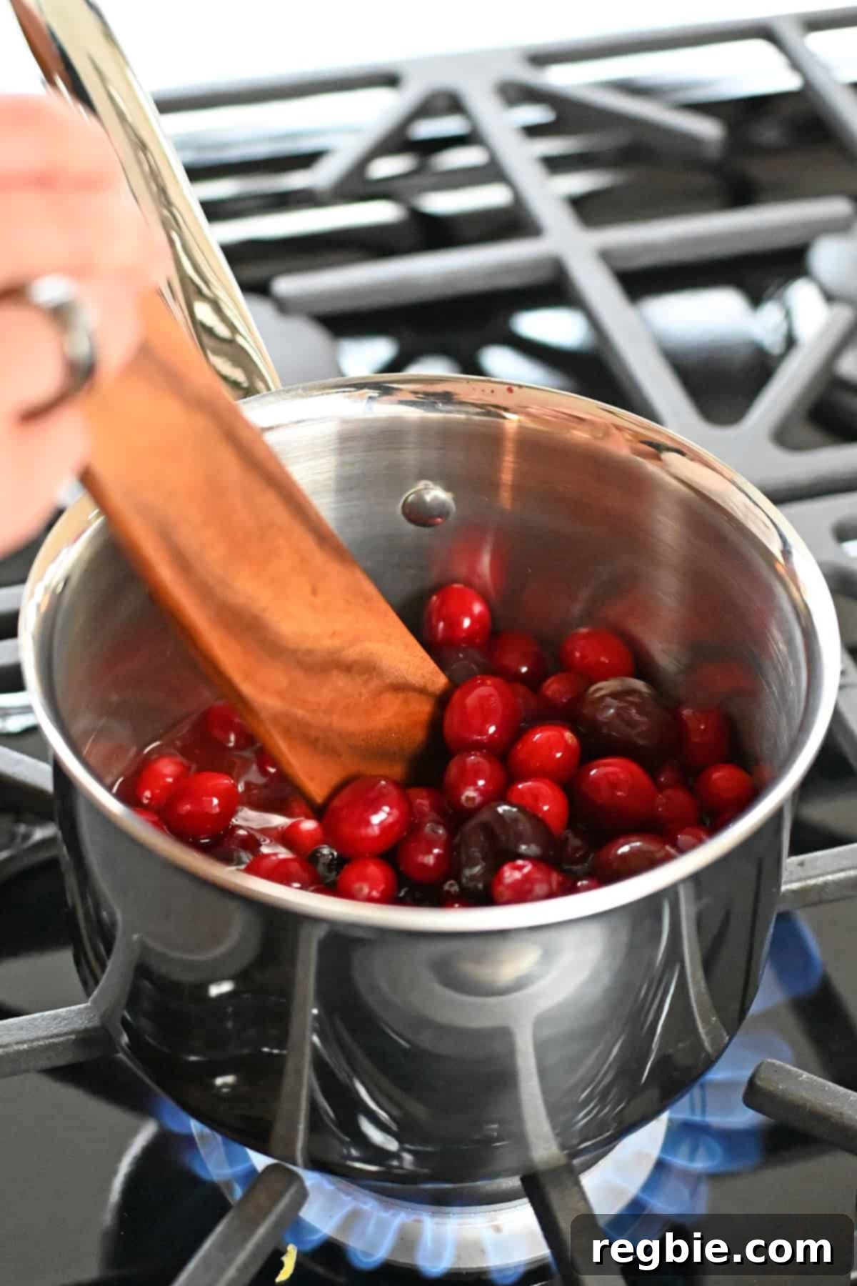 Stirring a saucepan filled with the ingredients for paleo cranberry cherry sauce on a gas burner as it comes to a boil.