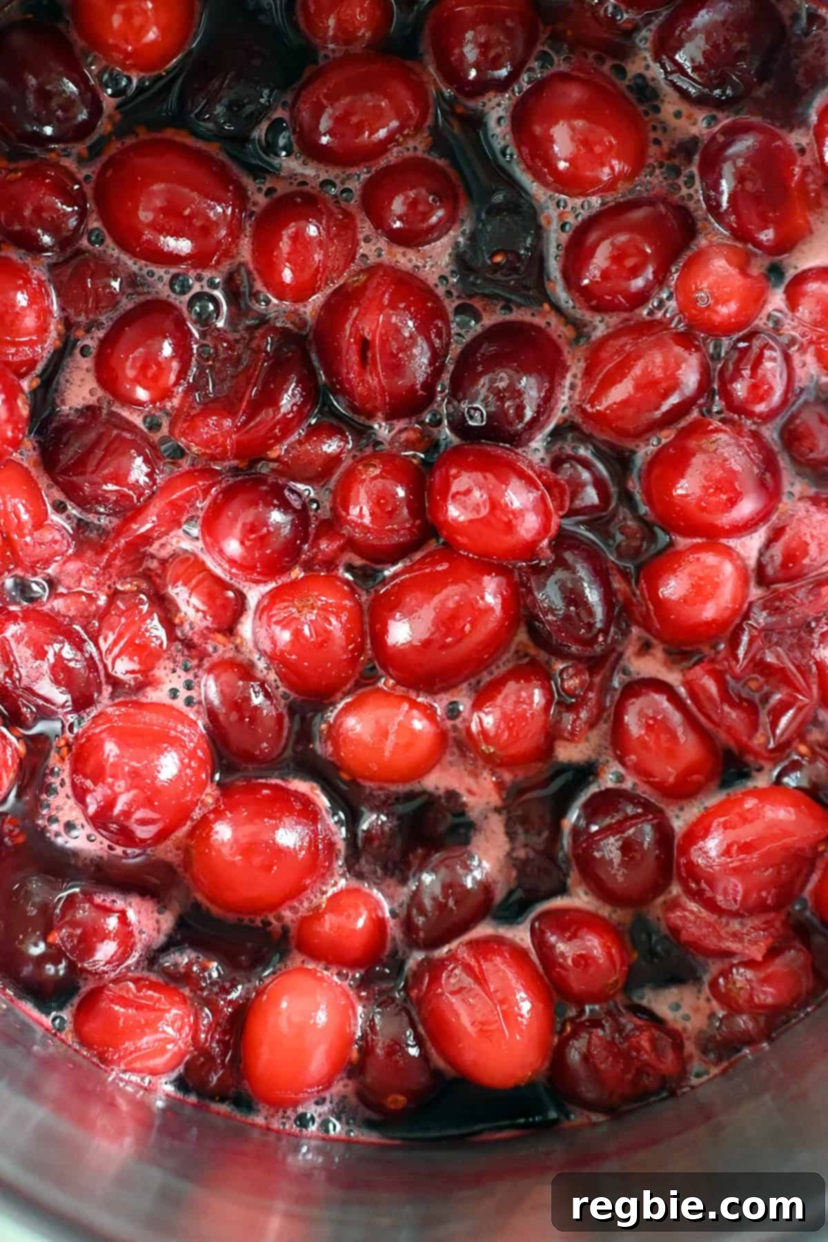 An overhead view of paleo cranberry sauce gently simmering in a saucepan, showing the fruit breaking down and the sauce thickening.