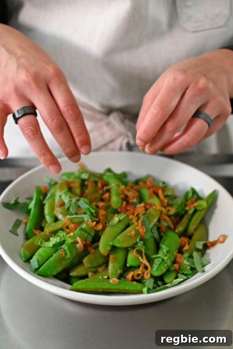 Speedy Southeast Asian Snap Pea Sensation 11 Scattering golden crispy shallots over a plate of stir-fried sugar snap peas, alongside fresh herbs.