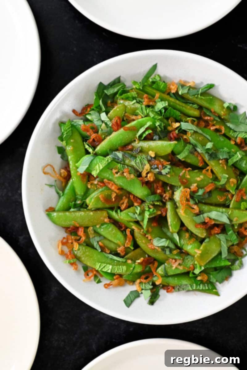 Speedy Southeast Asian Snap Pea Sensation 12 An overhead shot of a bowl of Asian sugar snap peas stir fry, generously topped with fresh herbs and crispy shallots, ready to be served.