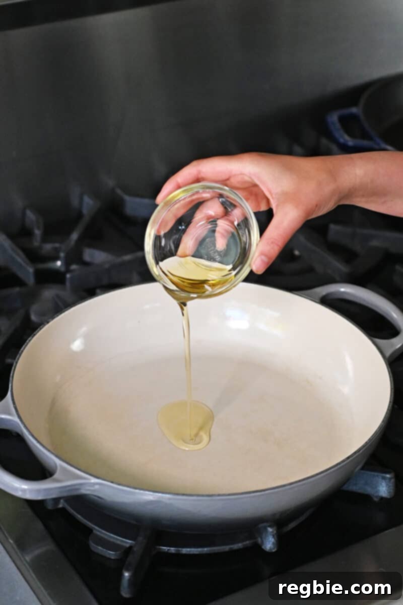 Speedy Southeast Asian Snap Pea Sensation 5 A hand is pouring a small bowl of avocado oil into a large enamel cast iron skillet, which is already hot on the stove.