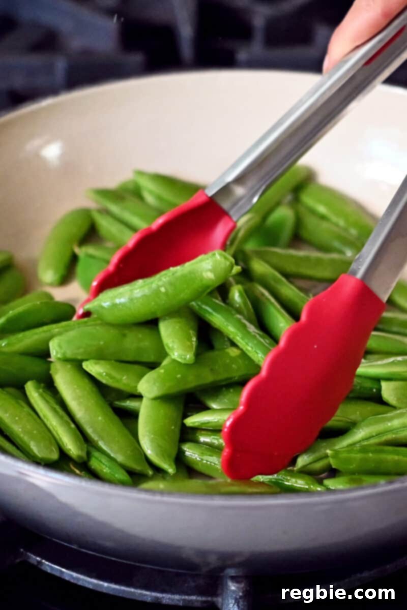 Speedy Southeast Asian Snap Pea Sensation 7 Tossing bright green sugar snap peas in a large skillet with a pair of tongs to ensure even cooking and searing.
