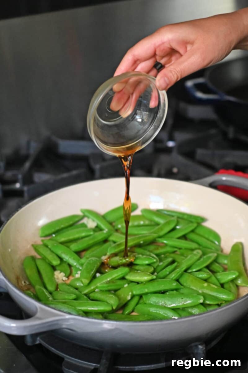 Speedy Southeast Asian Snap Pea Sensation 8 Pouring a small bowl of fish sauce into a skillet filled with brightly cooked sugar snap peas and fragrant minced garlic.