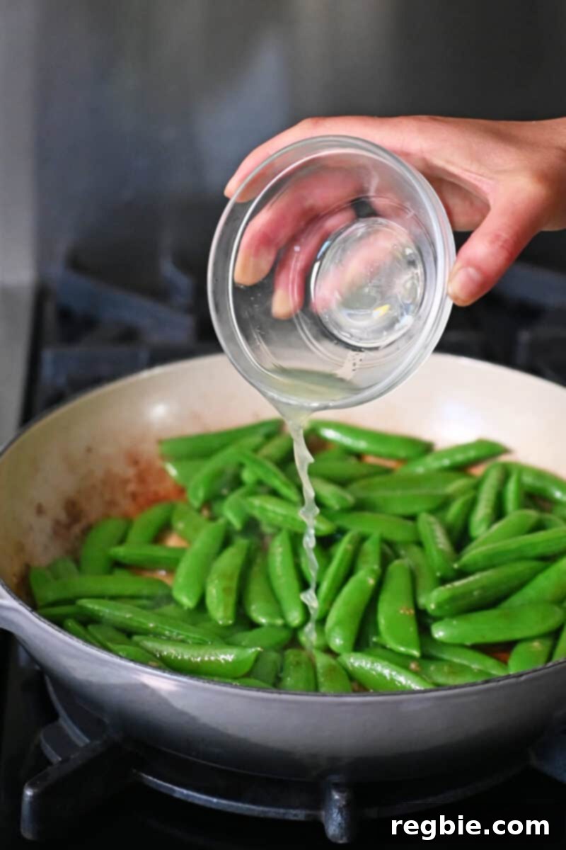 Speedy Southeast Asian Snap Pea Sensation 9 Pouring a small bowl of freshly squeezed lime juice into a skillet with sugar snap peas, garlic, and fish sauce, with the heat now off.