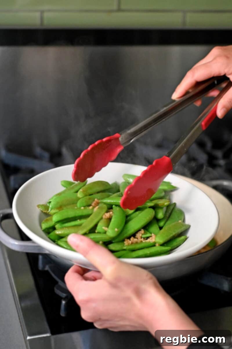 Speedy Southeast Asian Snap Pea Sensation 10 Using a pair of tongs to transfer sautéed sugar snap peas to a shallow off-white bowl for serving.