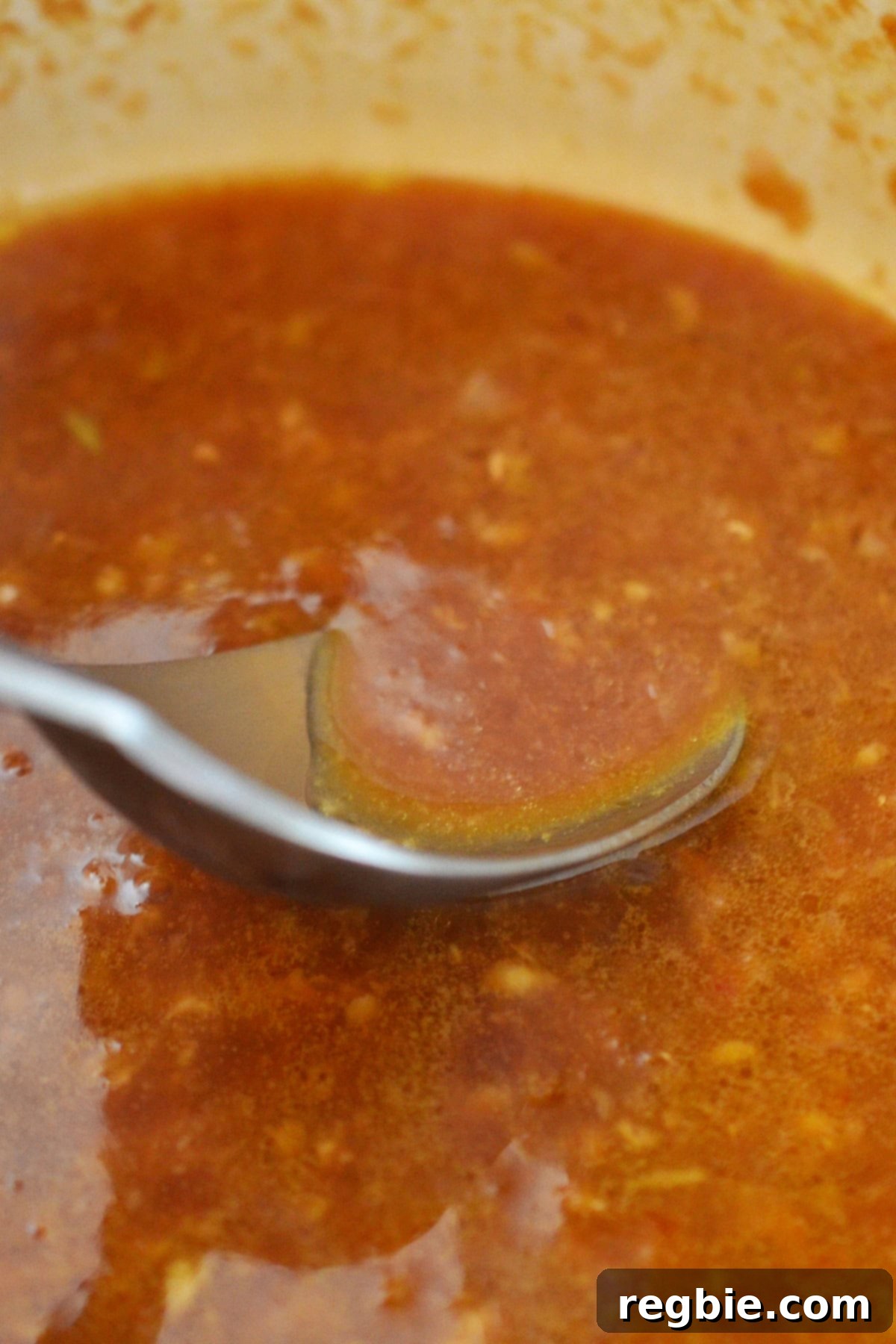 A spoon scooping up some Asian citrus dressing from a saucepan, showing its slightly thickened texture and rich color.