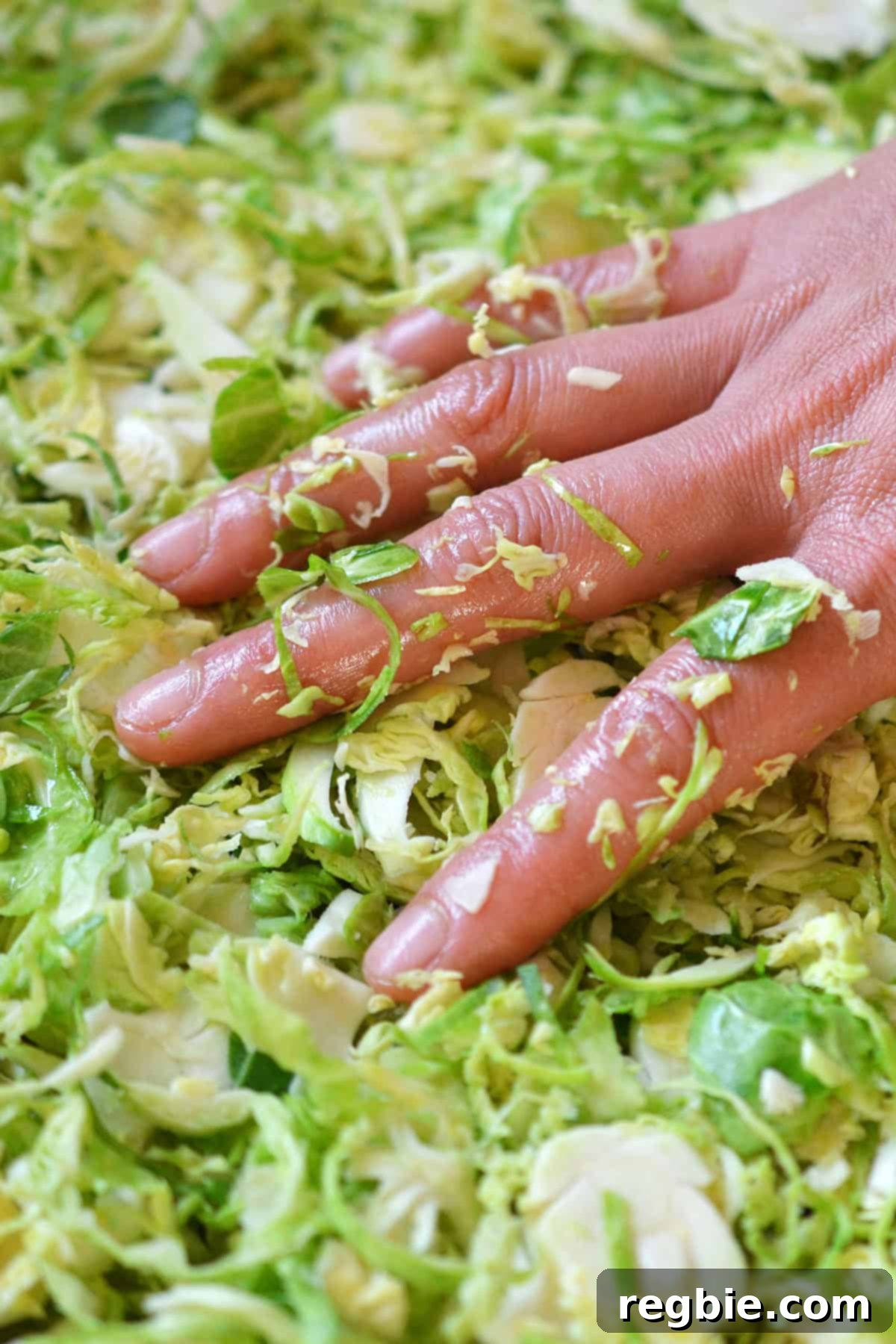 A hand carefully placing the seasoned shaved Brussels sprouts in a single layer on a rimmed baking sheet, preparing them for even roasting.