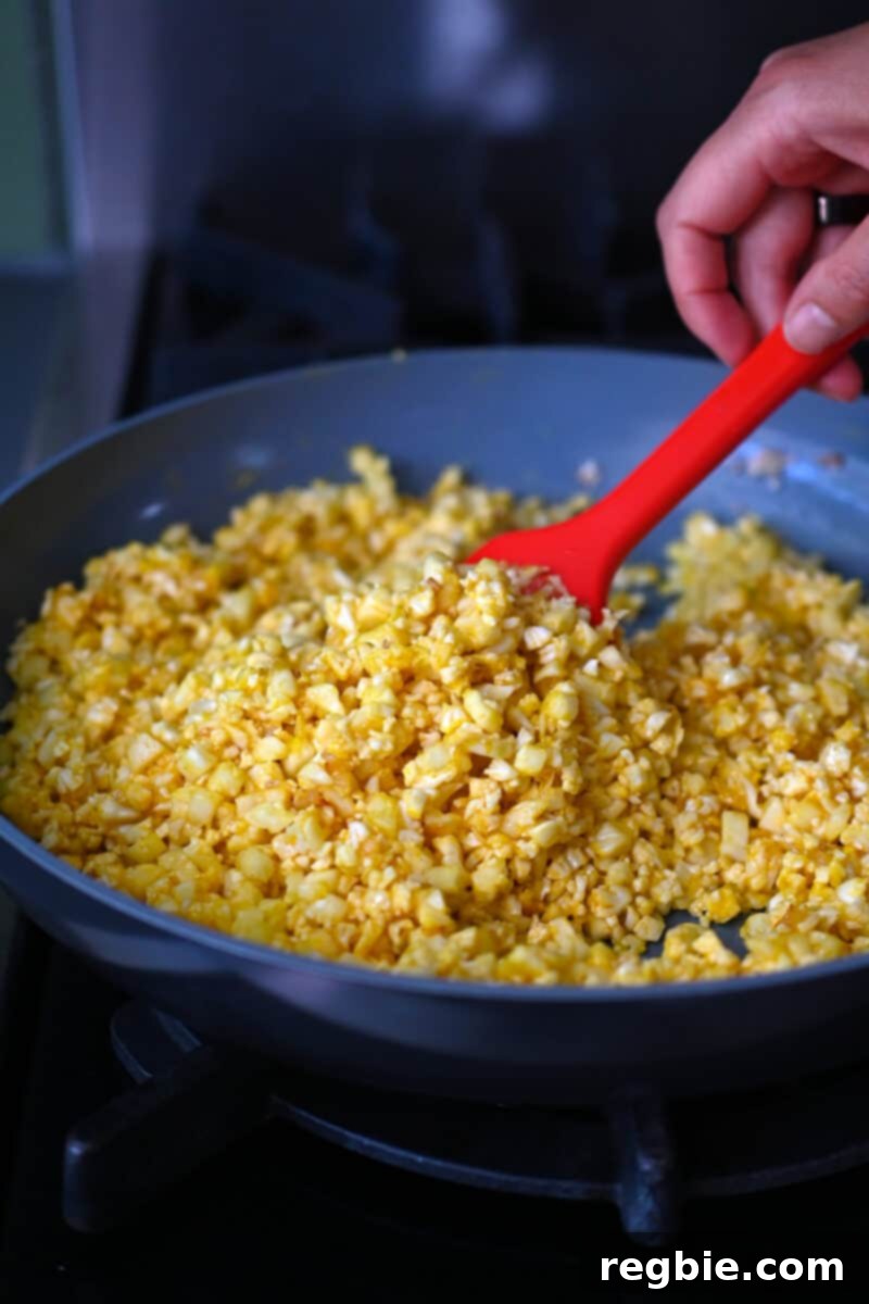 A skillet is filled with cauliflower rice coated with egg yolks, actively stir-frying to achieve a golden, crisp-tender texture.