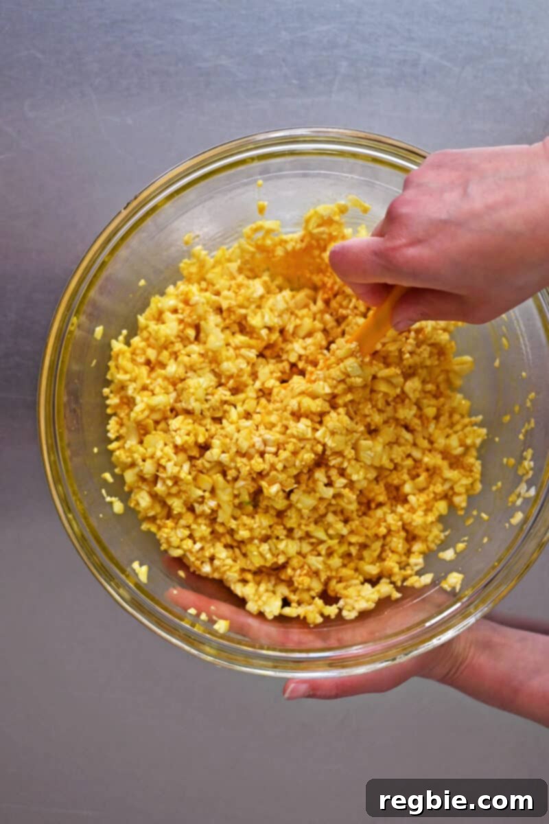 An overhead shot of cauliflower rice coated evenly with egg yolks and seasoning, ready for stir-frying to make golden cauliflower fried rice.