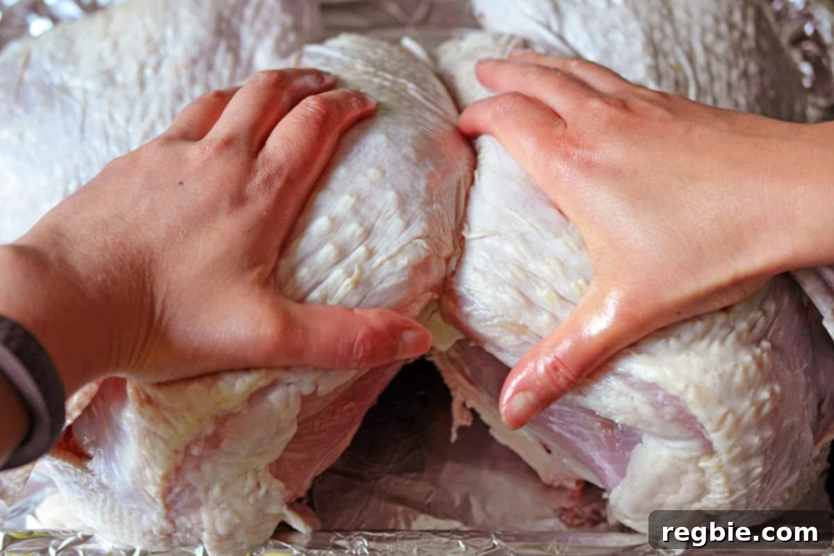 Firmly pressing down on the breast of a raw butterflied turkey to flatten it completely.
