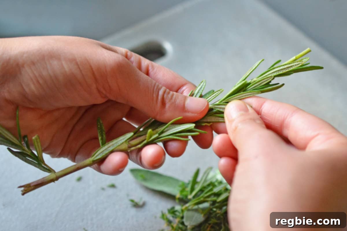 Two hands meticulously removing rosemary leaves from a fresh sprig for the herb butter.