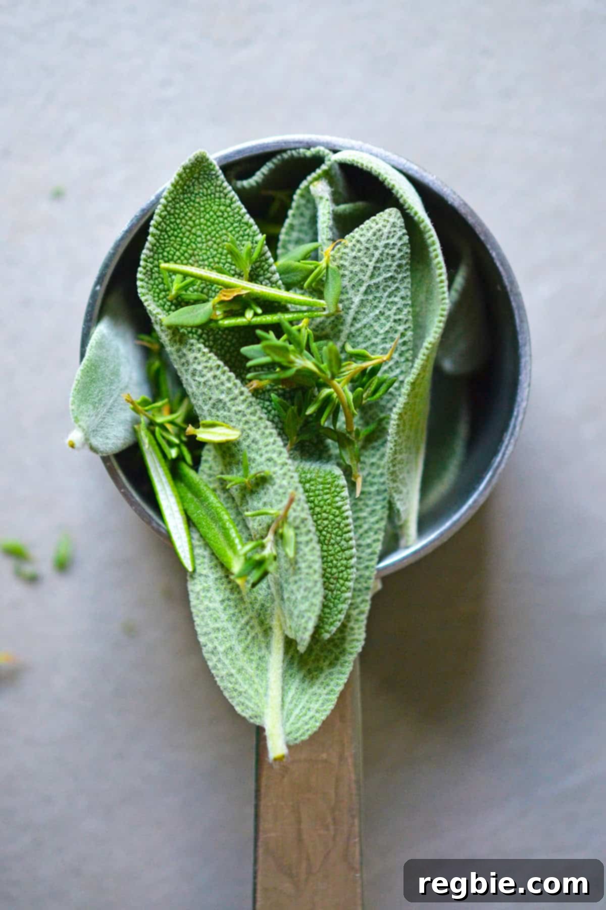 A measuring cup filled with fresh sage, thyme, and rosemary, ready to be minced.