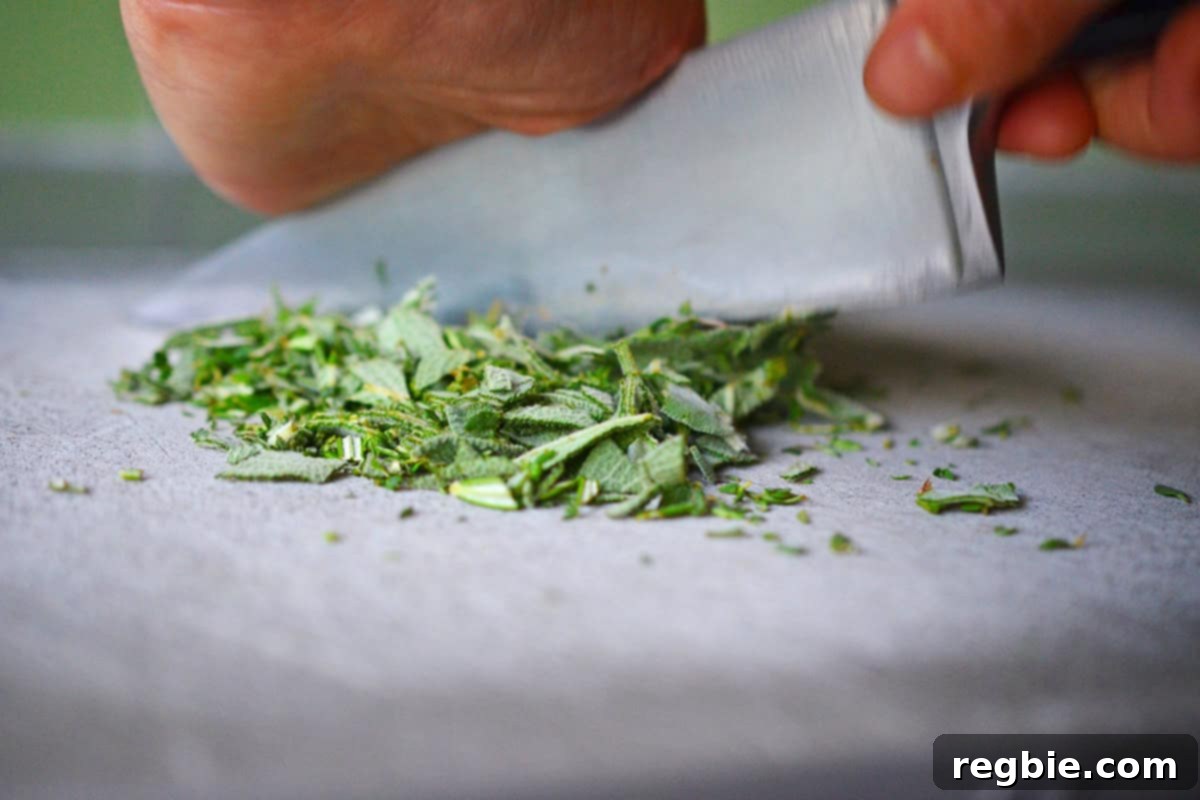 Finely mincing fresh herbs on a gray cutting board to prepare for compound butter.