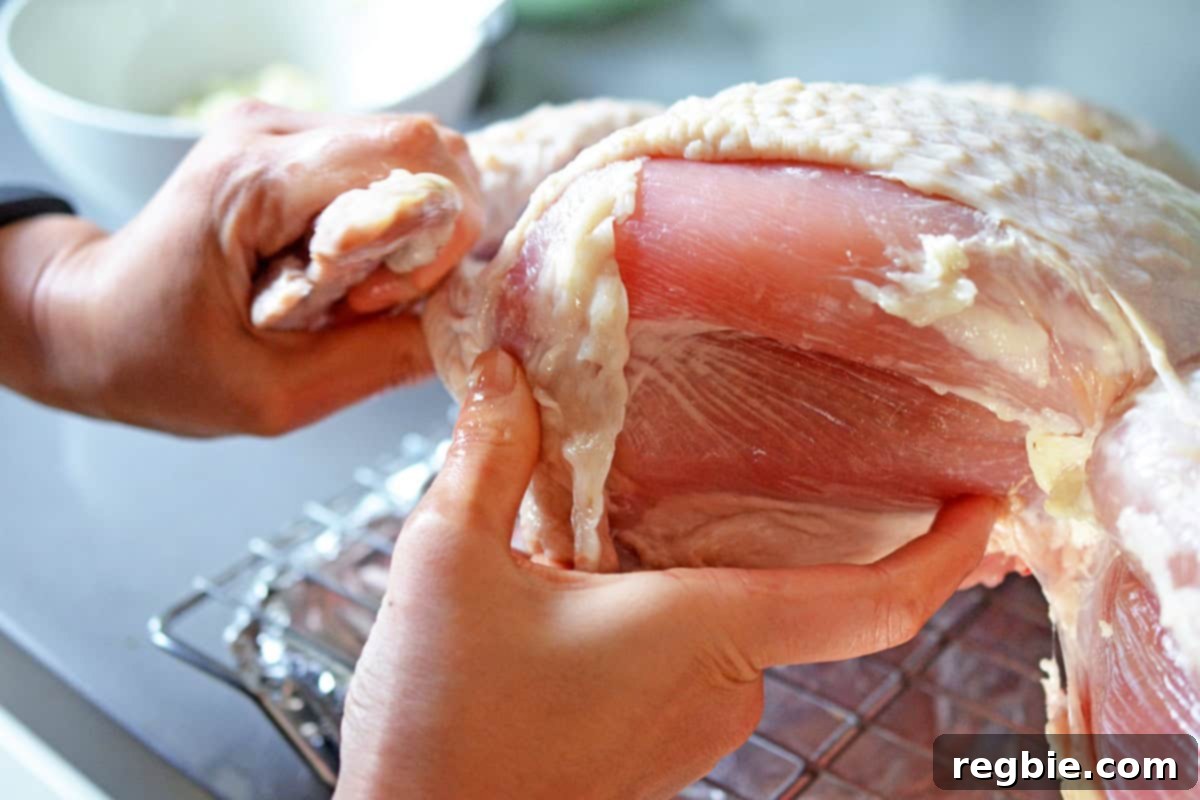 Using hands to spread herb butter under the skin of a raw, dry-brined spatchcock turkey, positioned on a wire rack.