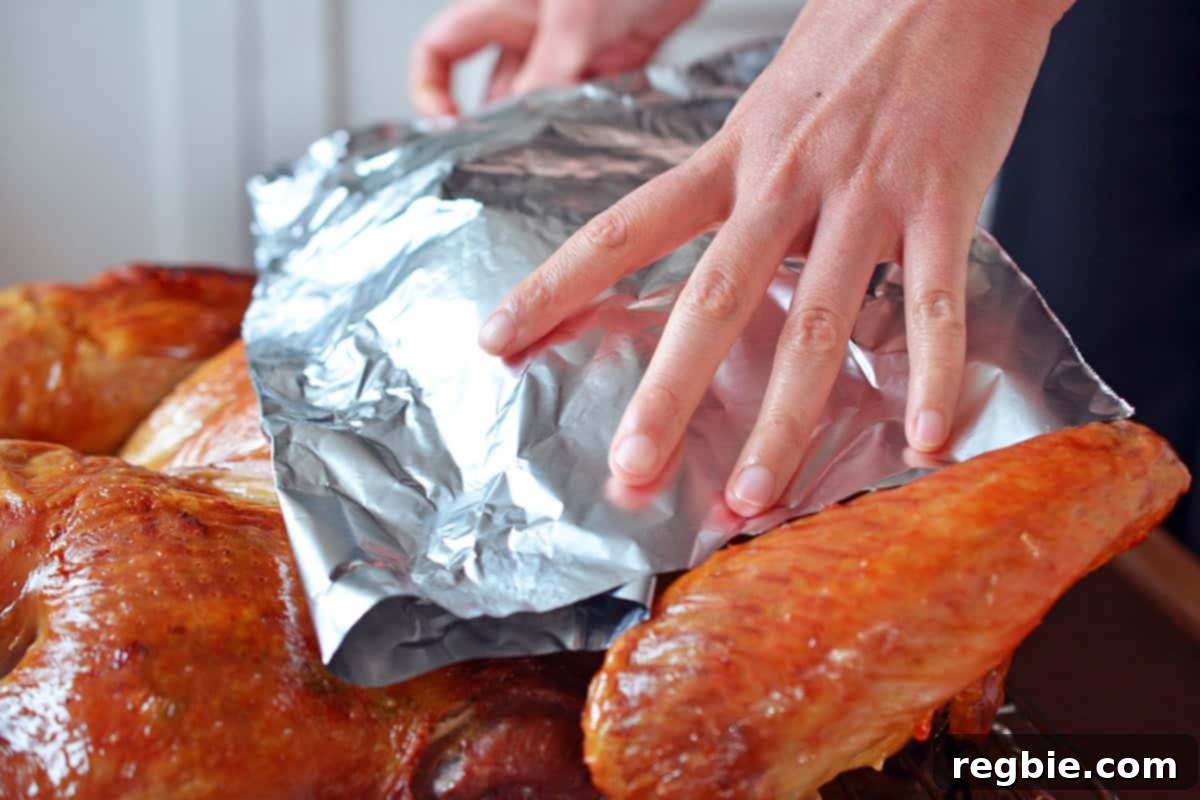 Placing aluminum foil loosely over the breast meat of a spatchcock turkey to prevent over-browning while it continues to roast.