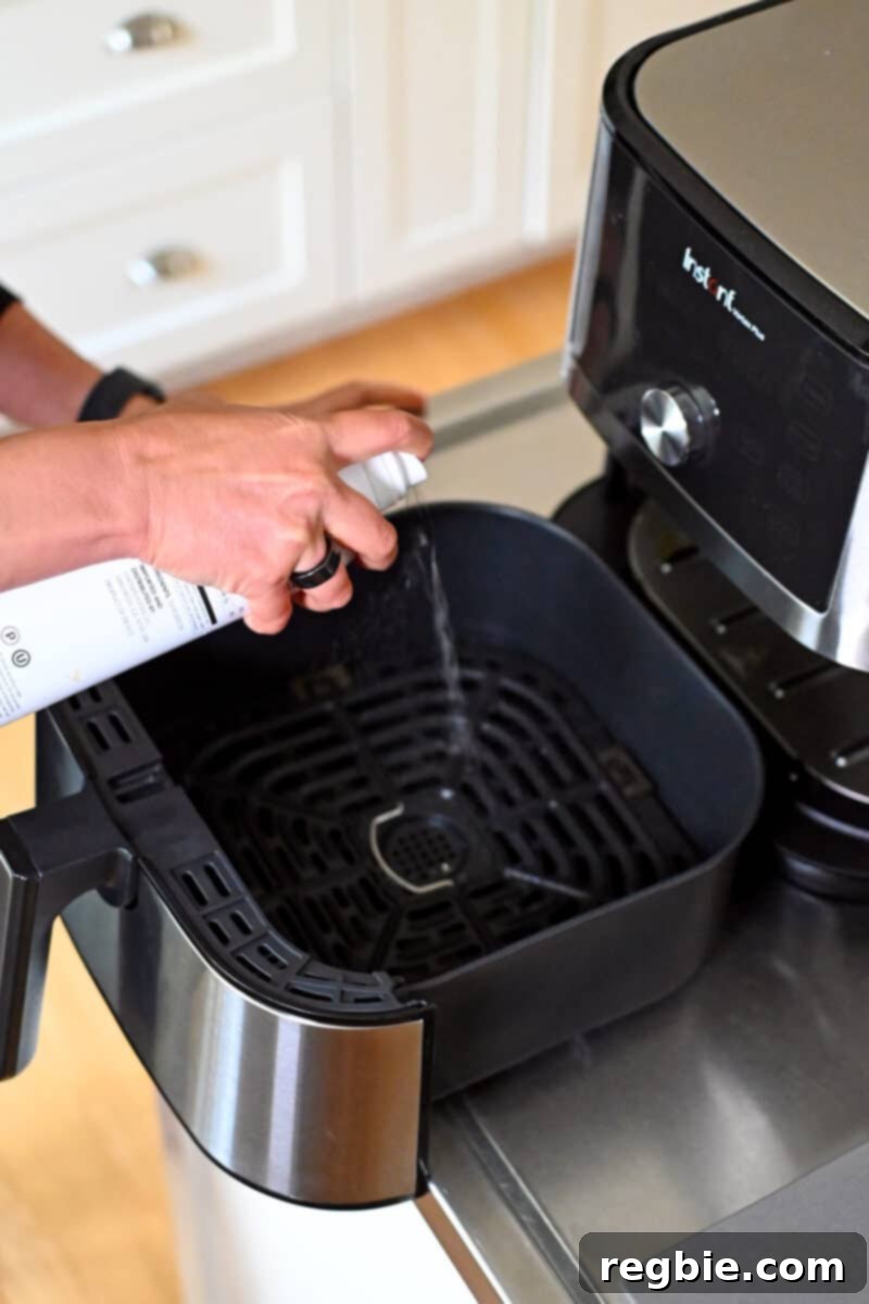 Avocado oil spray is being applied to the interior of an open air fryer basket, preparing it for cooking.