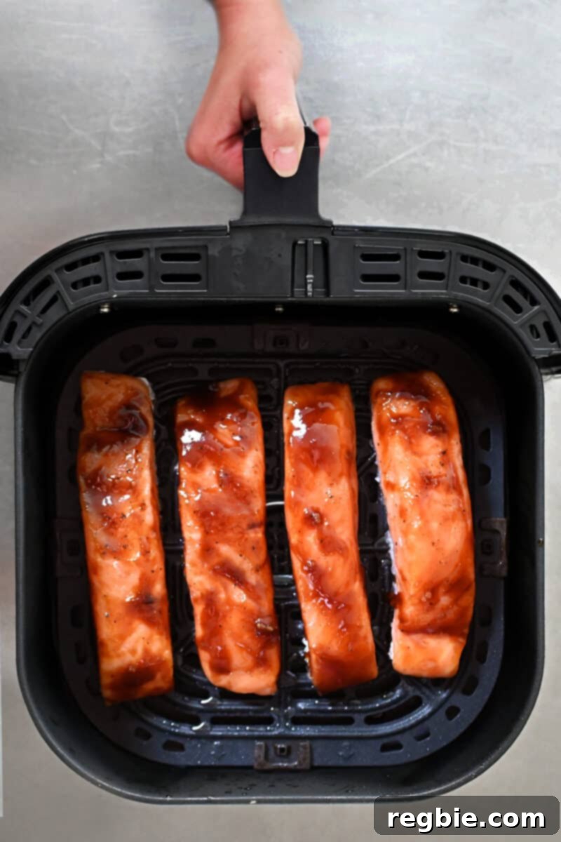 An overhead shot shows four glazed salmon fillets neatly arranged, skin-side down, in an open air fryer basket.