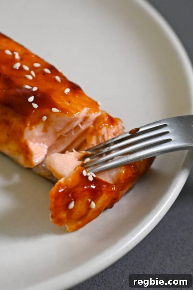 A fork gently separates the flaky flesh of an air fryer salmon fillet, demonstrating its moist and tender texture.