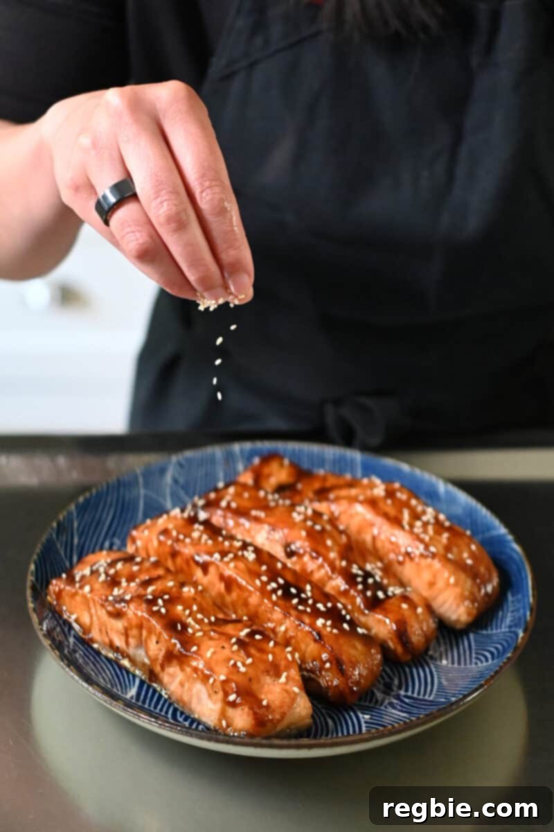 Toasted sesame seeds are being sprinkled over a plate of air fryer salmon fillets, adding a final touch.