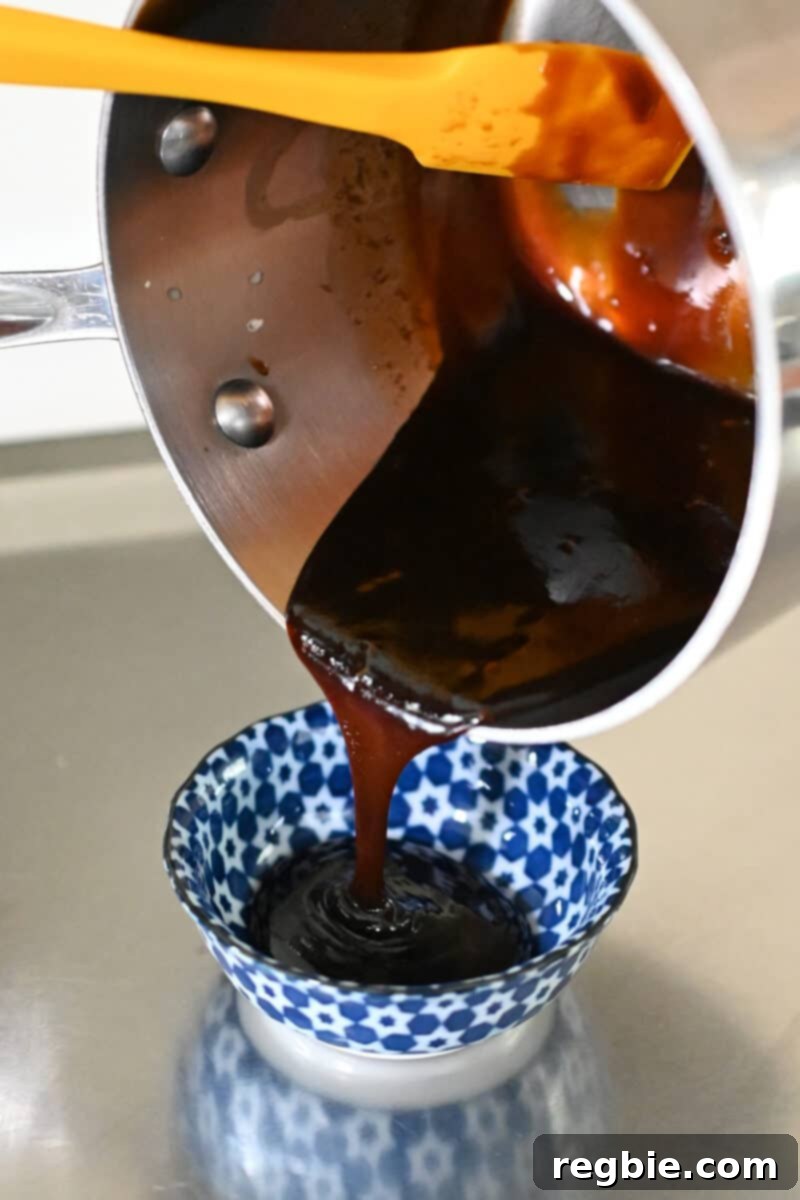 A small saucepan is used to pour a rich, simmering honey sriracha sauce into a smaller serving bowl.