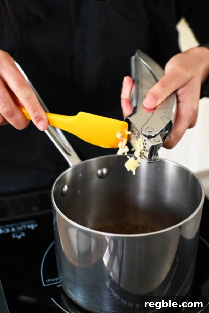 Minced garlic is being added to a small saucepan already containing coconut aminos, honey, and sriracha, the base for the glaze.