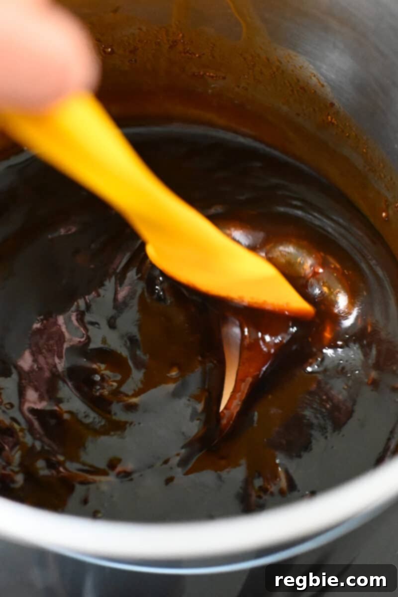 A close-up view of the honey sriracha sauce simmering in a saucepan, now noticeably thickened and glossy after adding the slurry.