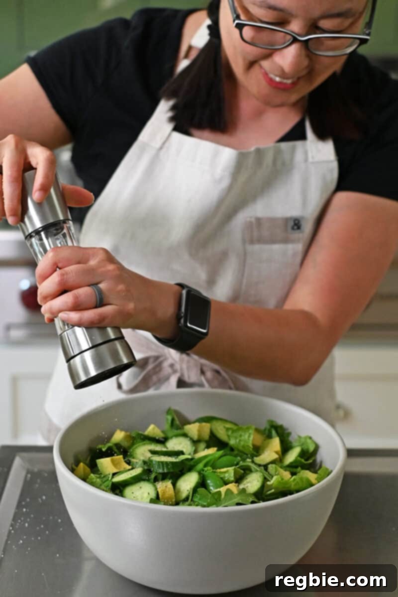 Whole30 Vegan Asian Chopped Salad 11 An Asian woman adding freshly cracked black pepper to a large, inviting bowl filled with a colorful array of chopped salad ingredients.