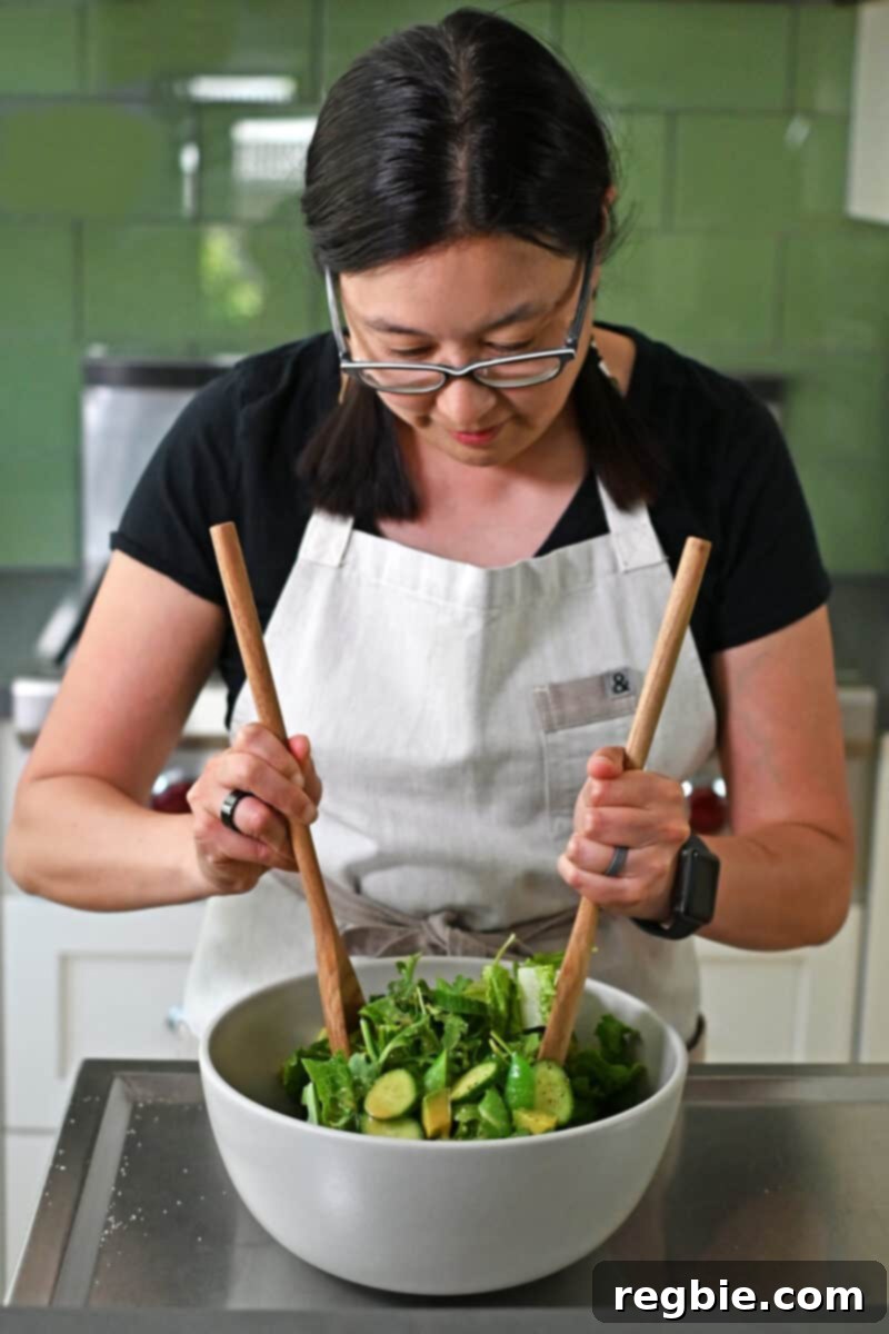 Whole30 Vegan Asian Chopped Salad 12 An Asian woman gracefully tossing a vibrant chopped salad with creamy sesame ginger dressing in a spacious white bowl, ensuring even coating.