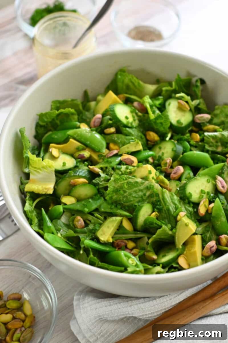 Whole30 Vegan Asian Chopped Salad 4 A close-up view of the finished Asian chopped salad in a white bowl, showing a vibrant mix of green salad leaves, perfectly cubed avocado, bright sugar snap peas, thinly sliced cucumbers, and crunchy pistachios, all glistening with sesame ginger dressing.