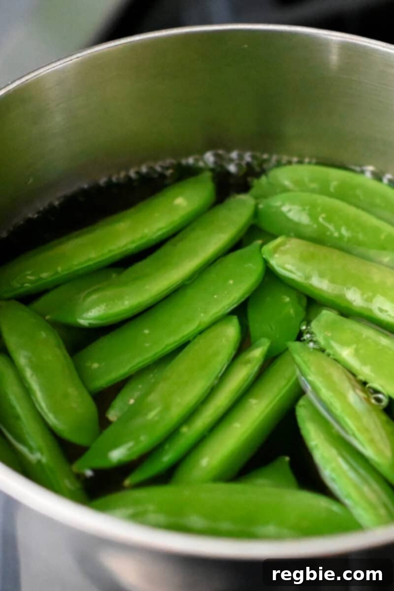 Whole30 Vegan Asian Chopped Salad 7 A small saucepan filled with vigorously boiling water, containing bright green sugar snap peas, demonstrating the blanching process.