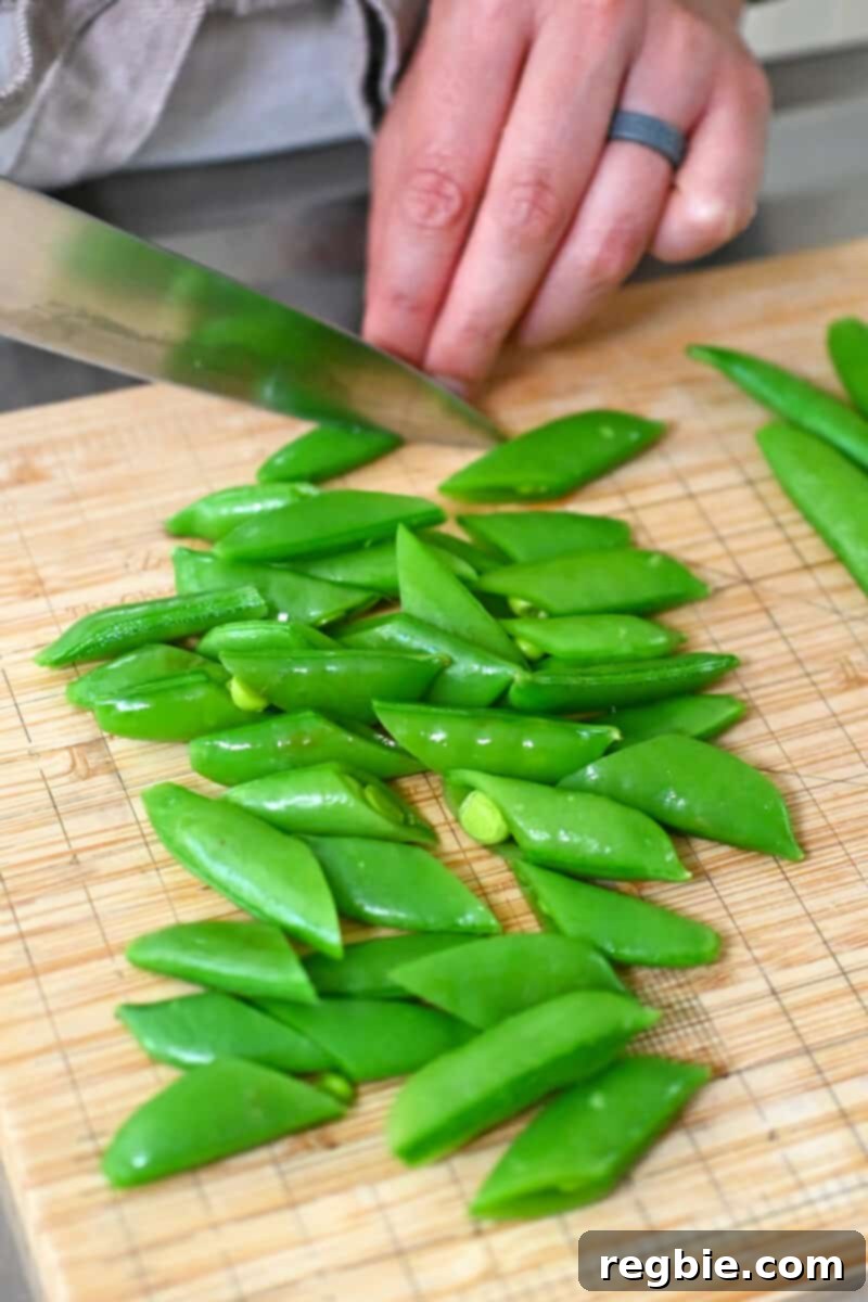 Whole30 Vegan Asian Chopped Salad 10 Chopping blanched sugar snap peas in half on a wooden cutting board, preparing them for the salad.