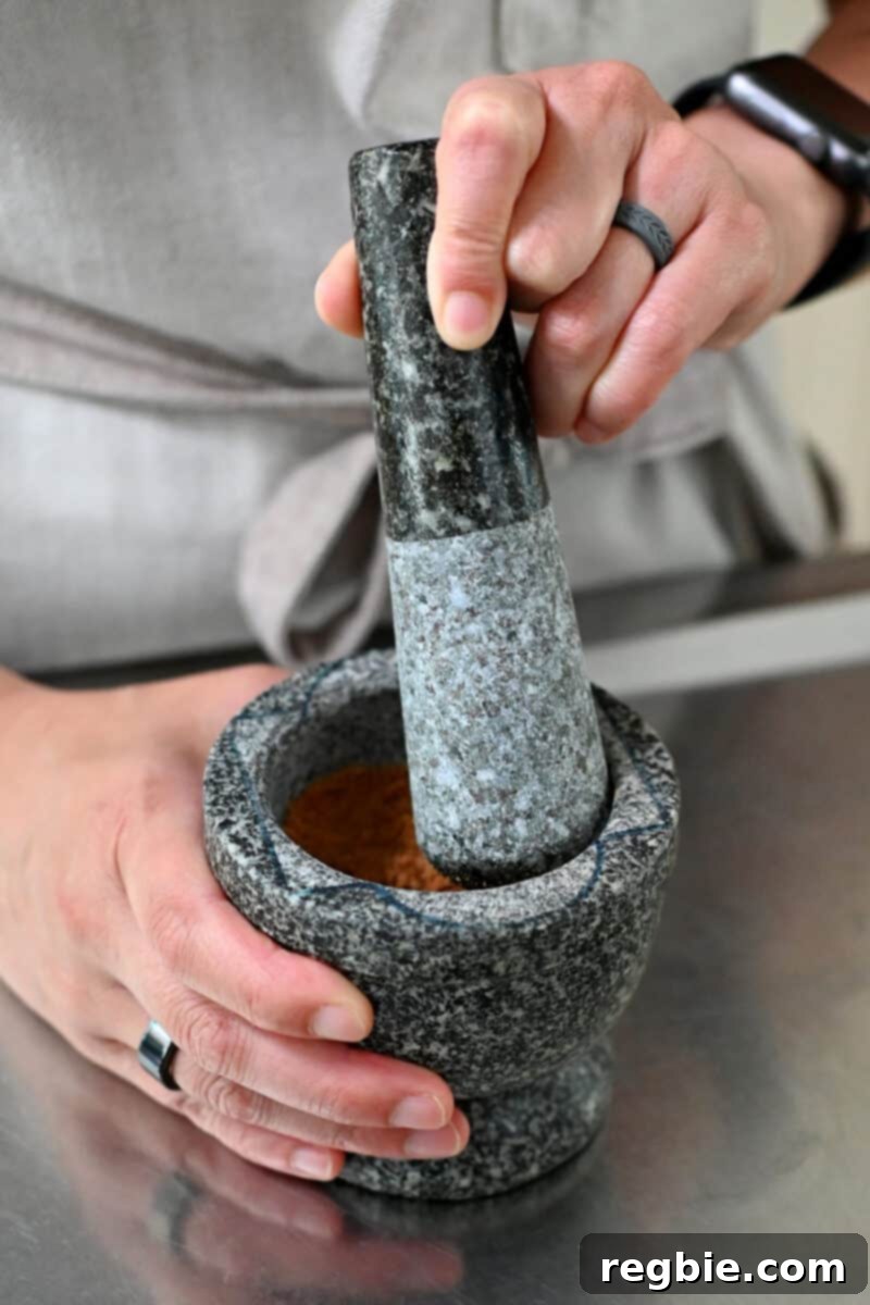 A close-up shot of paleo cookies being crushed in a traditional mortar and pestle, preparing the delicious topping for the cheesecake stuffed strawberries.