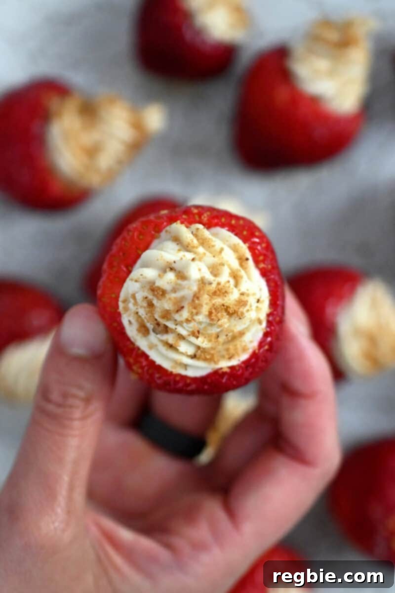 An inviting overhead shot focusing on the perfectly mounded cheesecake filling within a single strawberry, topped with crumbs, highlighting its delicious texture.