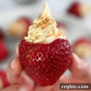 A hand is holding up a paleo and vegan cheesecake stuffed strawberry topped with gluten-free cookie crumbs, showcasing the delectable dessert.