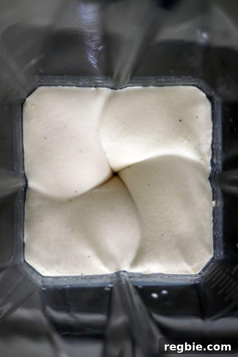An overhead shot revealing an open Vitamix blender, its contents a thick, creamy, and perfectly smooth vegan cheesecake filling, ready for the next step.