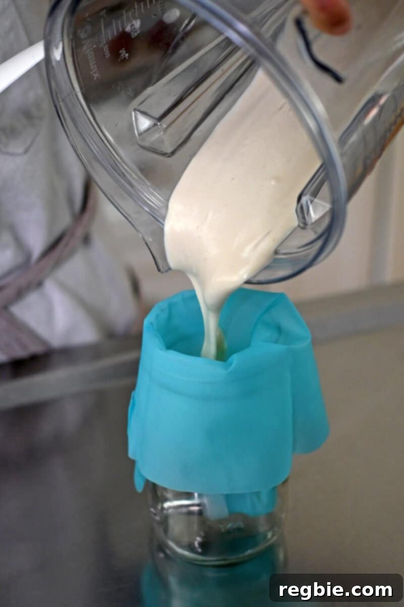 A close-up view of the paleo and vegan cheesecake mixture being carefully poured into a vibrant blue silicone piping bag, set within a jar for stability.