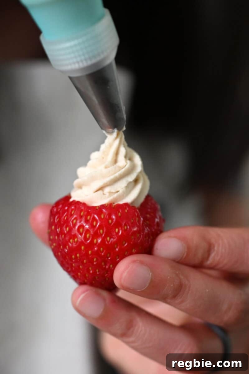 A pastry bag is expertly piping creamy cheesecake filling into a hollowed-out strawberry, demonstrating the precision and elegance of the dessert preparation.